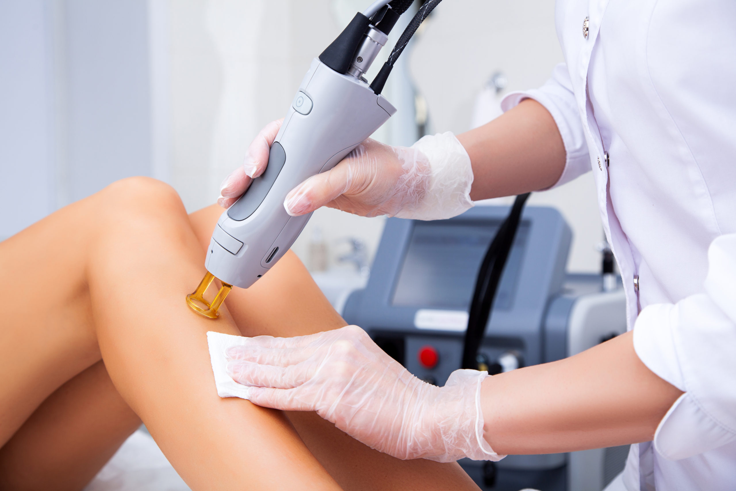 Close-up of a female cosmetologist in a medical coat making a young woman a procedure laser hair removal for leg. Cosmetology, ionization, diamond procedures.